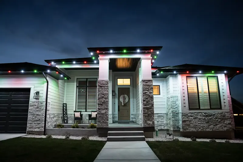 Single-story home at night with red, green and white lights spaced along the roofline and porch