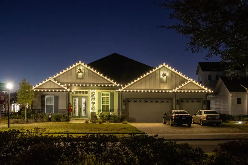 Single-story home with warm white roofline lights and wreaths on both gables